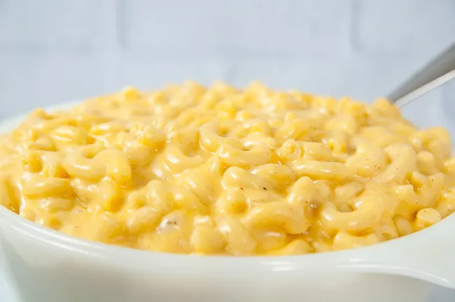 A spoon full of Instant Pot mac and cheese being lifted out of a white dish in a white kitchen