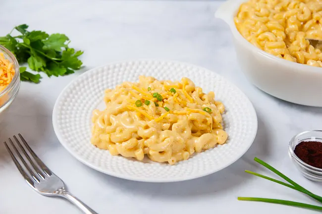 A white bowl and a white plate full of creamy macaroni and cheese that was made in the pressure cooker.