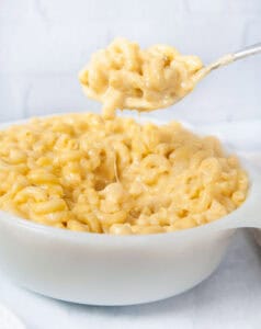 A spoon full of Instant Pot mac and cheese being lifted out of a white dish in a white kitchen