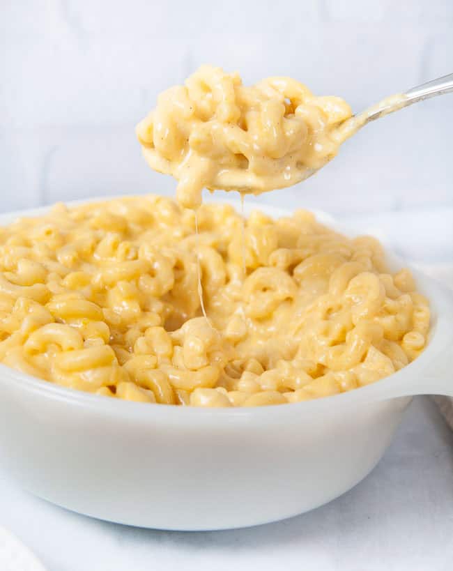 A spoon full of Instant Pot mac and cheese being lifted out of a white dish in a white kitchen