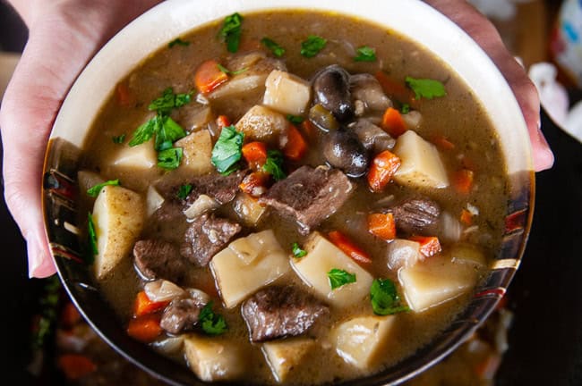 Hands holding a bowl of beef stew