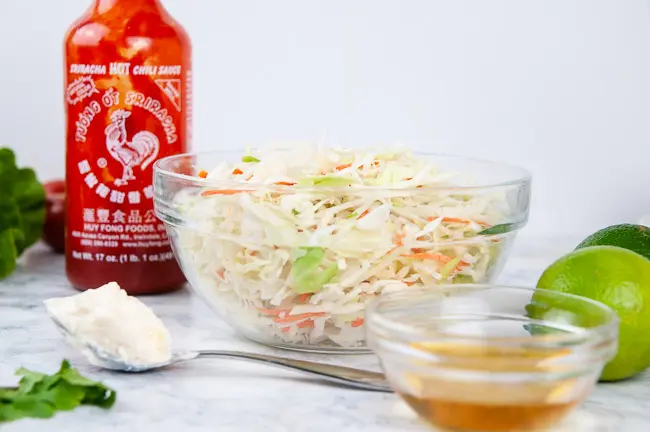 Ingriedients for sweet and spicy coleslaw: sriracha, mayo, honey, lime, and shredded cabbage and carrots