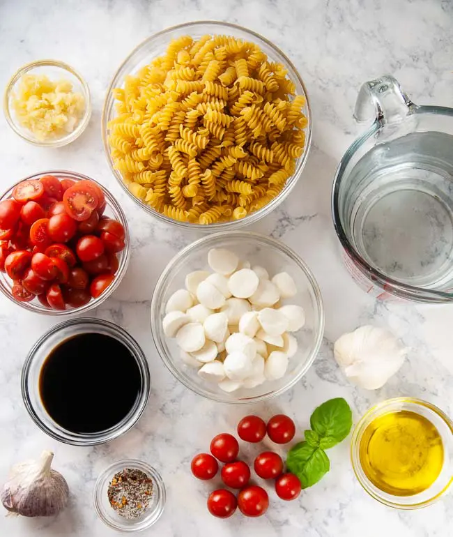 Ingredients for Instant Pot Caprese Pasta: rotini, cherry tomatoes, garlic, basil, mozzarella, balsamic vinegar, olive oil, and water