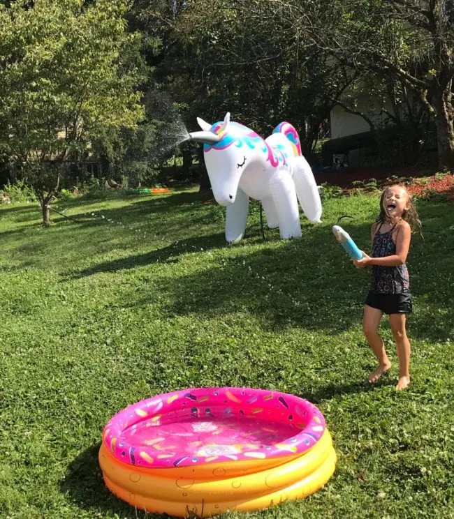 kid playing outside with a unicorn sprinkler and pink sprinkle inflatable pool