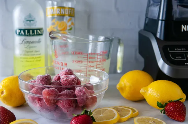 Ingredients for boozy strawberry lemonade slushies: frozen strawberries, limoncello, vodka, and lemonade