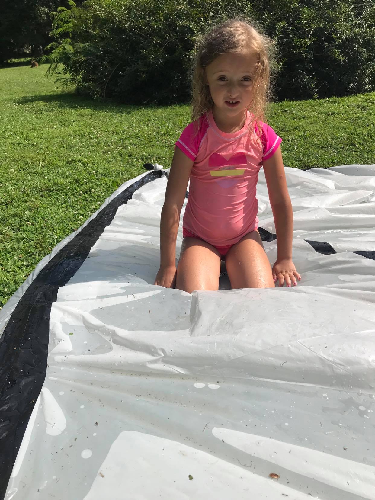 Little girl in pink swim shirt on a water filled plastic tarp,