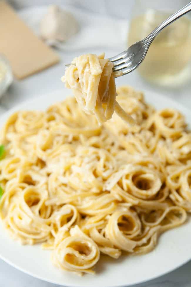 A fork twirling fettuccine alfredo above a plate