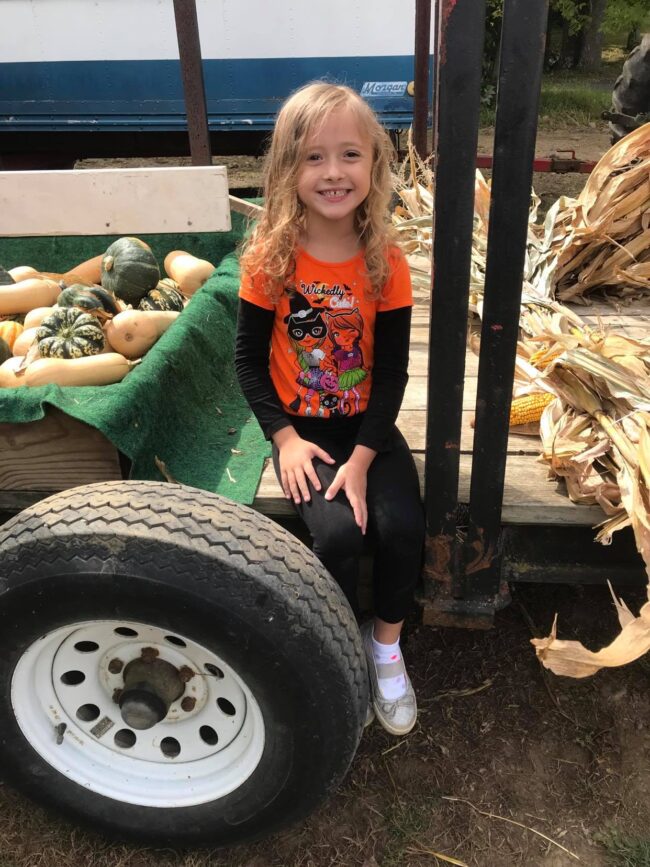 School aged girl sitting on a tractor full of gourds and corn husks