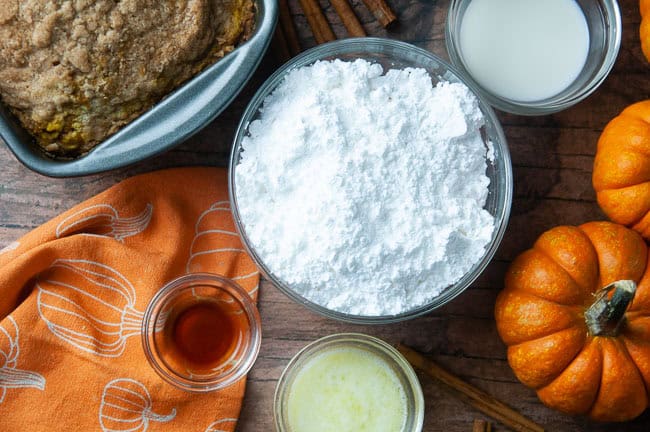 Bowls with powdered sugar, milk, melted butter, and vanilla sit next the baked loaf, ready to be turned into icing.