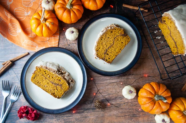 Two slices of cinnamon swirl pumpkin bread sit on brown rimmed plates on a wood table set for fall. The pumpkin bread makes a delicious breakfast or sweet treat.