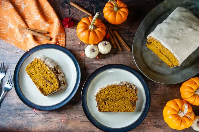 Two slices of cinnamon swirl pumpkin bread sit on brown rimmed plates on a wood table set for fall. The pumpkin bread makes a delicious breakfast or sweet treat.