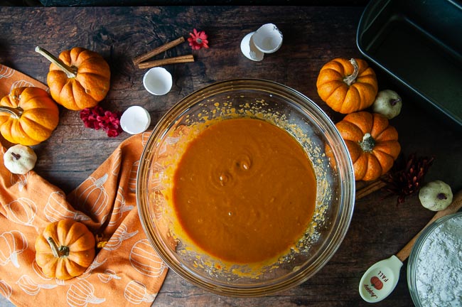 The wet ingredients get mixed together first to make a batter which is shown in a clear glass bowl on wood with pumpkins and the dry ingredients
