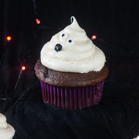 Ghost cupcakes on a black background with orange twinkle lights make a bootiful treat for Halloween.