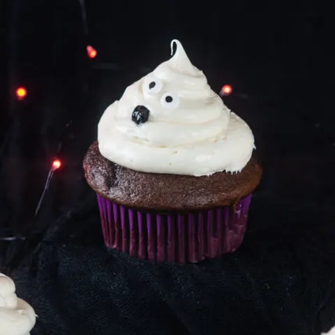 Ghost cupcakes on a black background with orange twinkle lights make a bootiful treat for Halloween.