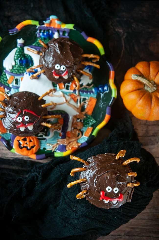 A chocolate cupcake decorated like a spider with pretzel legs and candy eyes for Halloween on black
