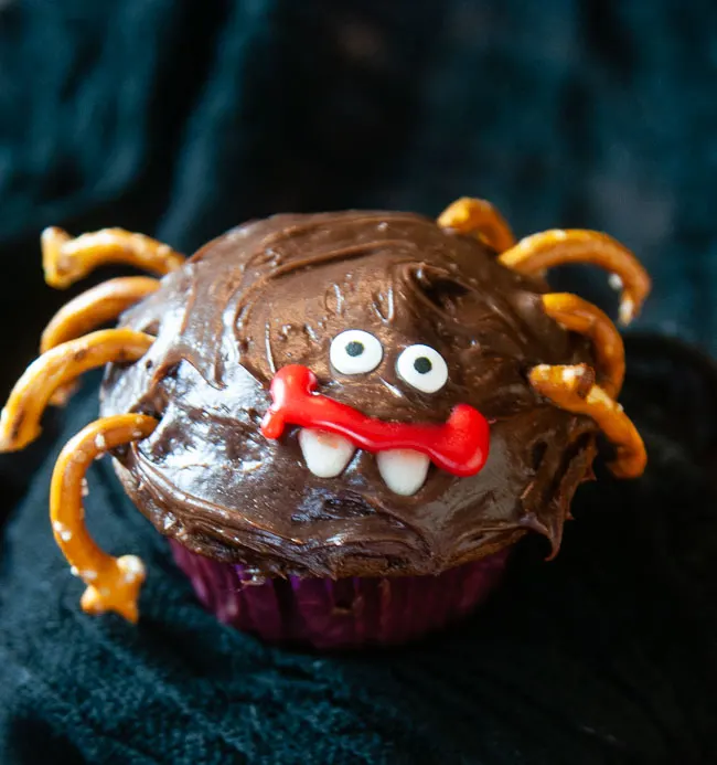 A chocolate cupcake decorated like a spider with pretzel legs and candy eyes for Halloween on black