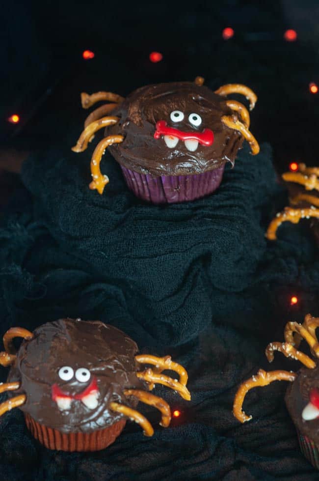 A chocolate cupcake decorated like a spider with pretzel legs and candy eyes for Halloween on black