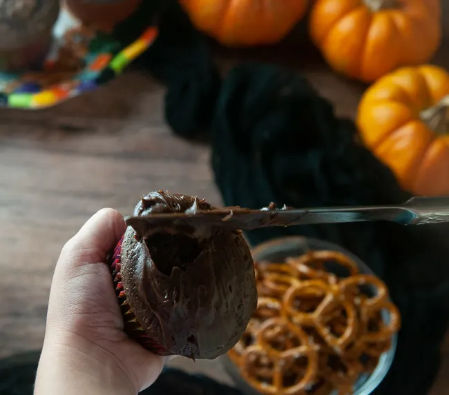 A child using a butterknife to frost a chocolate cupcake