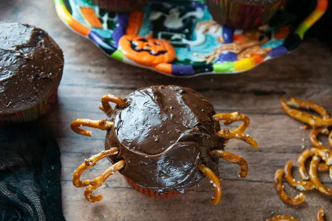 The beginnings of spider cupcakes- chocolate cupcakes with pretzel spider legs on wood. Push the pretzel pieces into the cupcakes to make the spider legs.