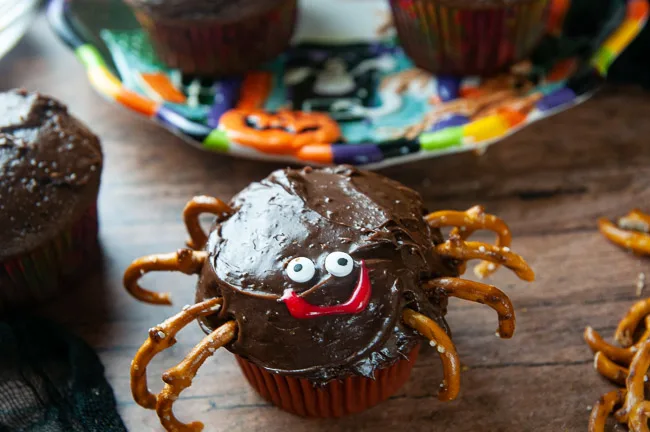 A chocolate cupcake decorated like a spider with pretzel legs and candy eyes for Halloween on black