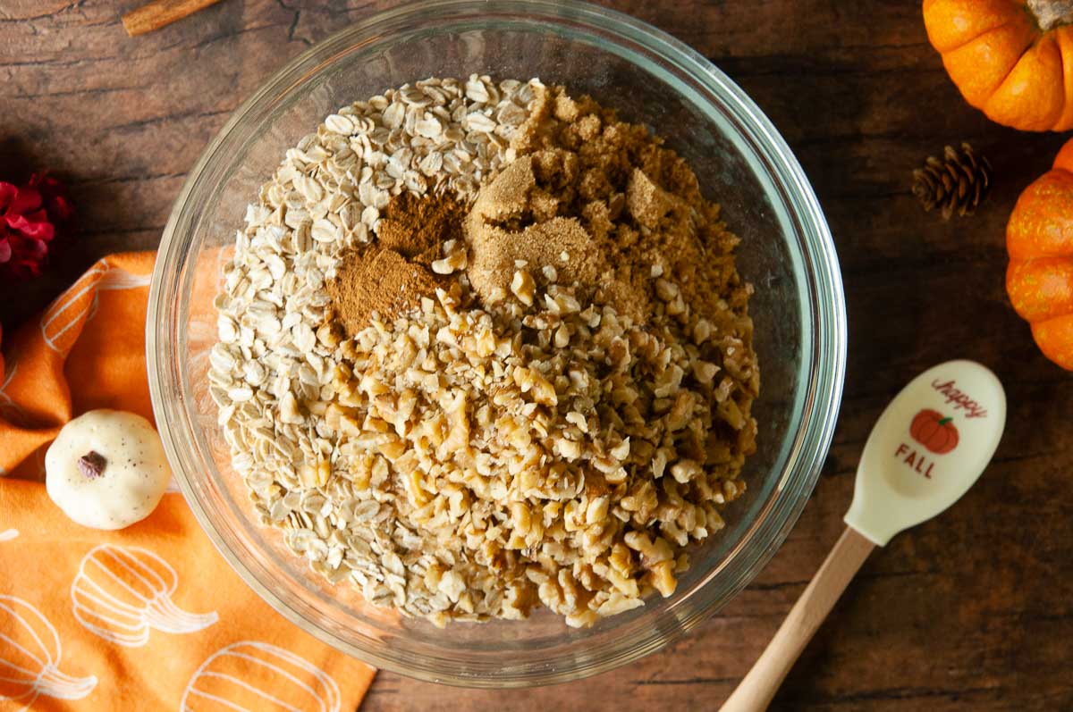 A bowl of oats, spices, walnuts and brown sugar sit on wood waiting for you toss them together