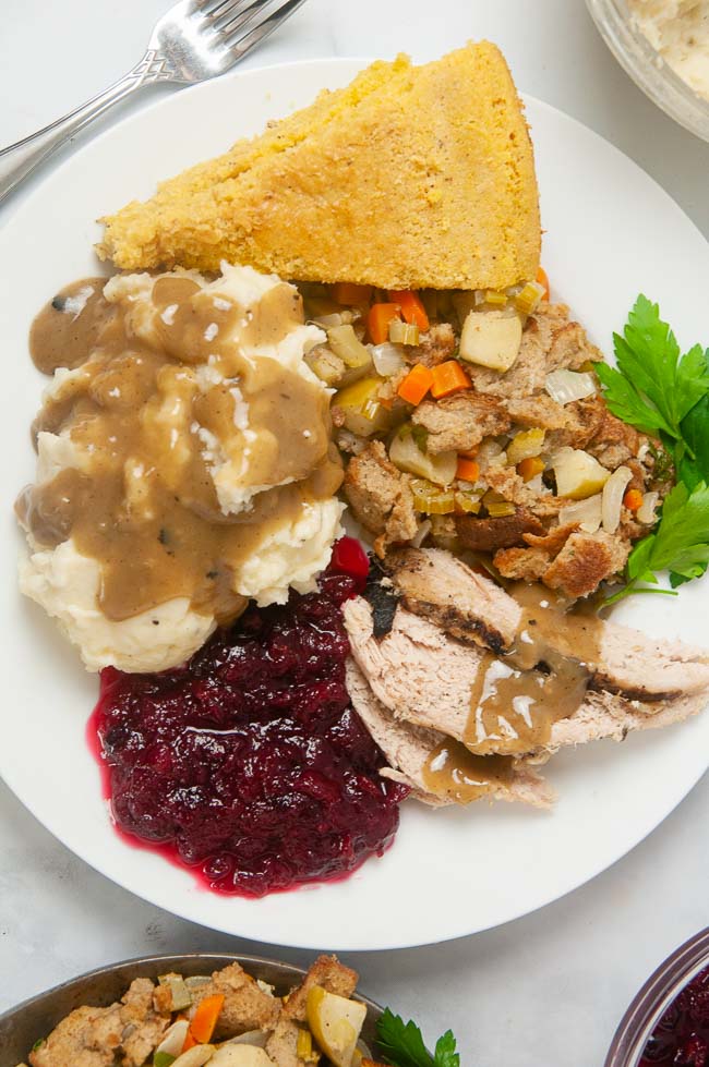 Turkey sliced on a plate with gravy, mashed potatoes, stuffing, cranberry sauce and cornbread.