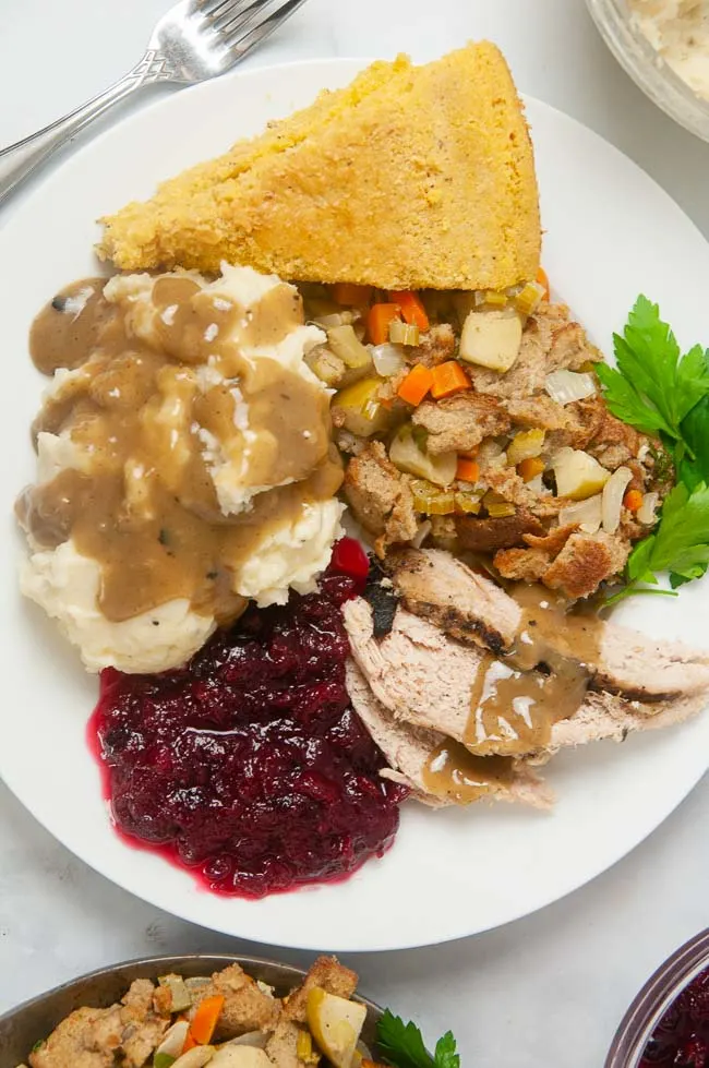 Turkey sliced on a plate with gravy, mashed potatoes, stuffing, cranberry sauce and cornbread.