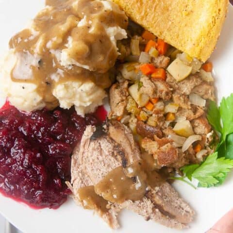 Turkey sliced on a plate with gravy, mashed potatoes, stuffing, cranberry sauce and cornbread.