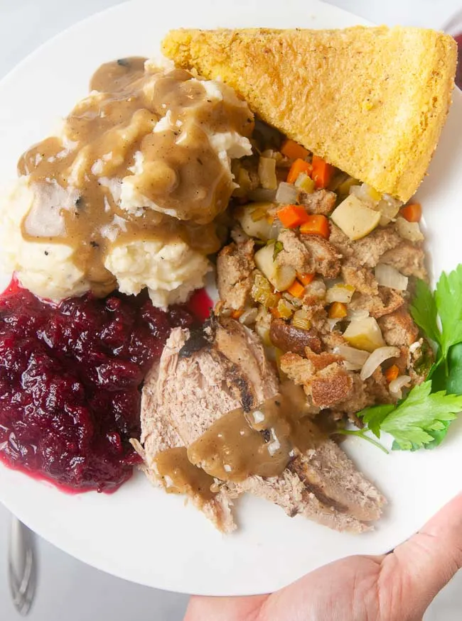 Turkey sliced on a plate with gravy, mashed potatoes, stuffing, cranberry sauce and cornbread.