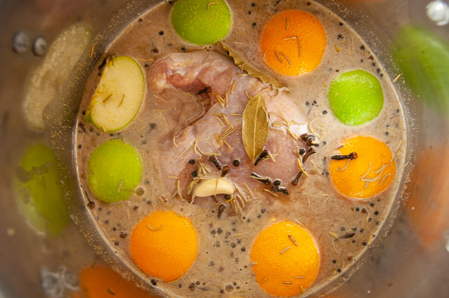 Turkey breast in a stock pot of liquid with oranges, spices, and apples