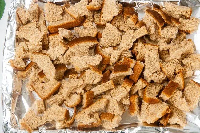 A cookie tray lined with foil full of torn bread cubes