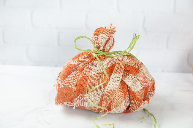 A plaid burlap pumpkin with raffia and ribbon tied around the stem.