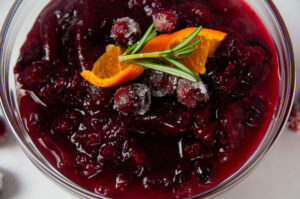 A clear bowl of Instant Pot Cranberry Sauce surrounded by cranberries on white. It is a bright, citrusy holiday side dish.