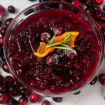 A clear bowl of Instant Pot Cranberry Sauce surrounded by cranberries on white. It is a bright, citrusy holiday side dish.