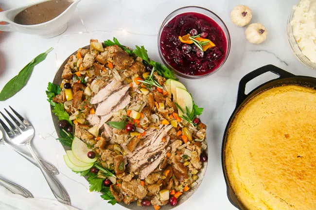 No turkey dinner is complete without cranberry sauce! A silver serving platter loaded with turkey and stuffing with a bowl of cranberry sauce on the side.