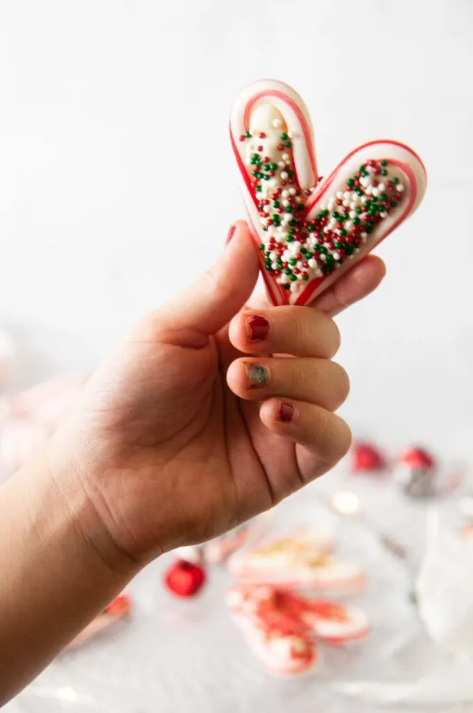 A child's hand holds a candy cane heart filled with chocolate and sprinkles