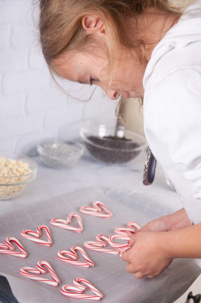 A little girl arranging candy canes like hearts on a cookie sheet