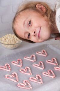 A little girl smiling over a tray of candy cane hearts