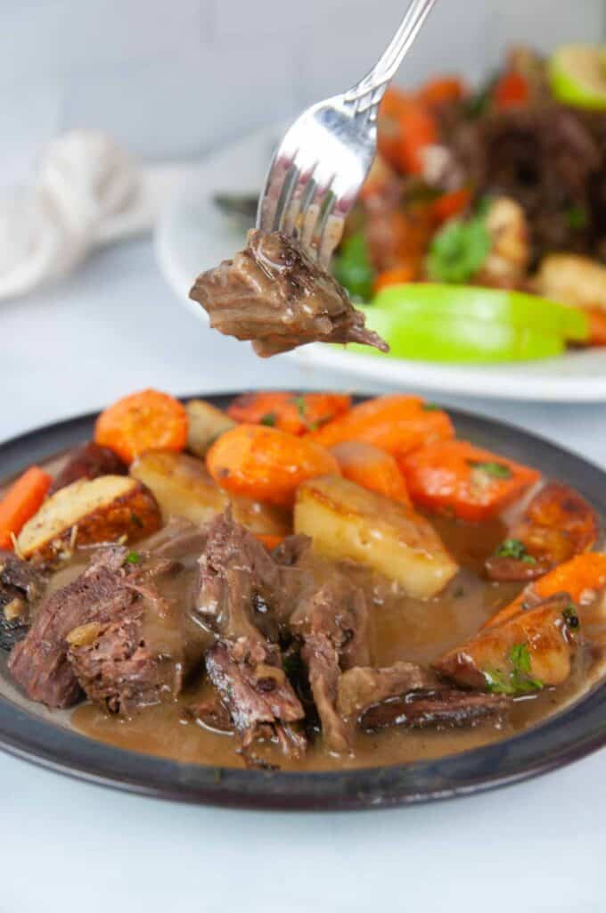 A forkful of tender Instant Pot Roast beef is slathered in apple cider gravy and served with roasted carrots and potatoes.