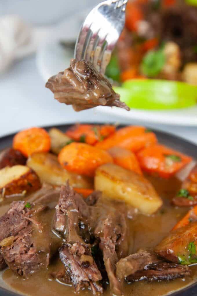 A forkful of tender Instant Pot Roast beef is slathered in apple cider gravy and served with roasted carrots and potatoes. 