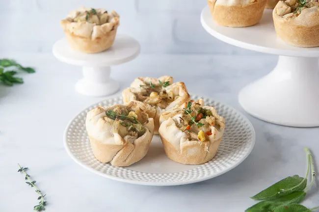Mini chicken pot pies on white platters in a white kitchen. These pot pies are a kid and freezer friendly way to use up leftover chicken or turkey.
