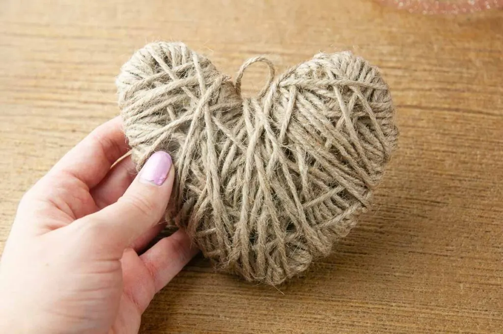 A hand holding a DIY twine heart craft done being wrapped in twine but not yet embellished.