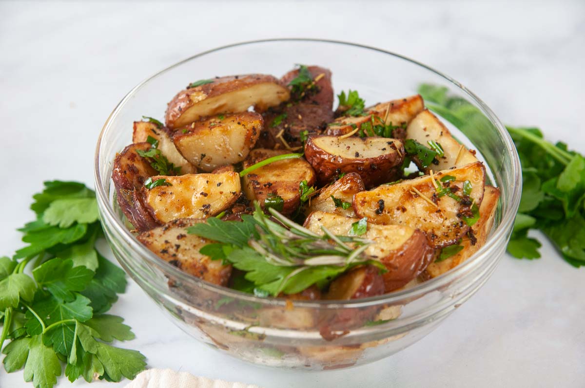 Garlic and Herb Roasted Red Potatoes in a clear glass bowl with lots of fresh herbs