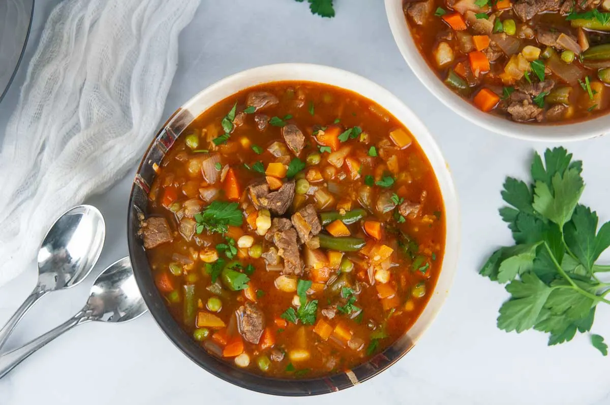 2 bowls of hearty Instant Pot vegetable beef soup ready for a cozy dinner on a white background.