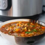 Instnat Pot Vegetable Beef soup is the perfect make ahead dinner. A bowl of it shown in front of the Instant Pot.