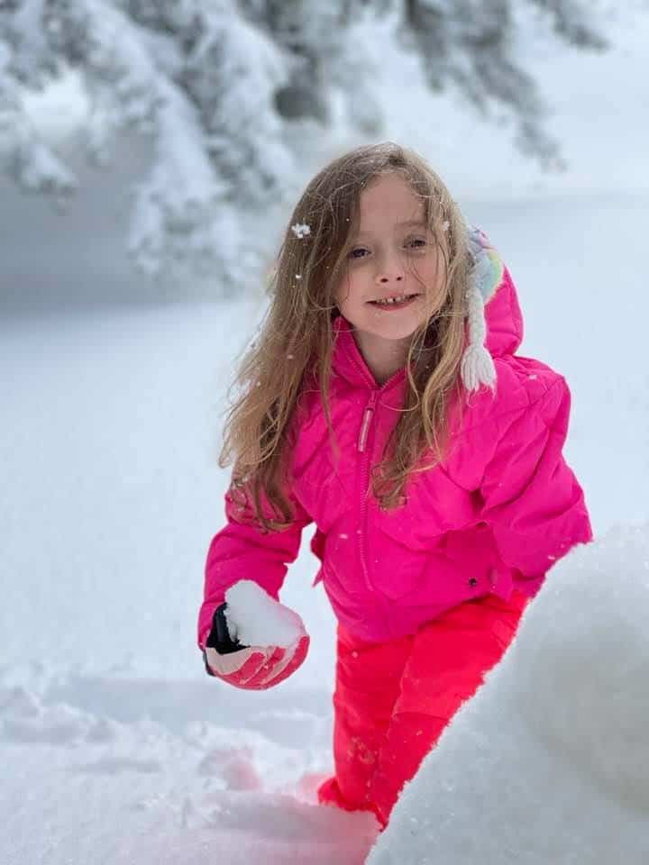 Elementary school girl in pink snow gear playing in deep snow