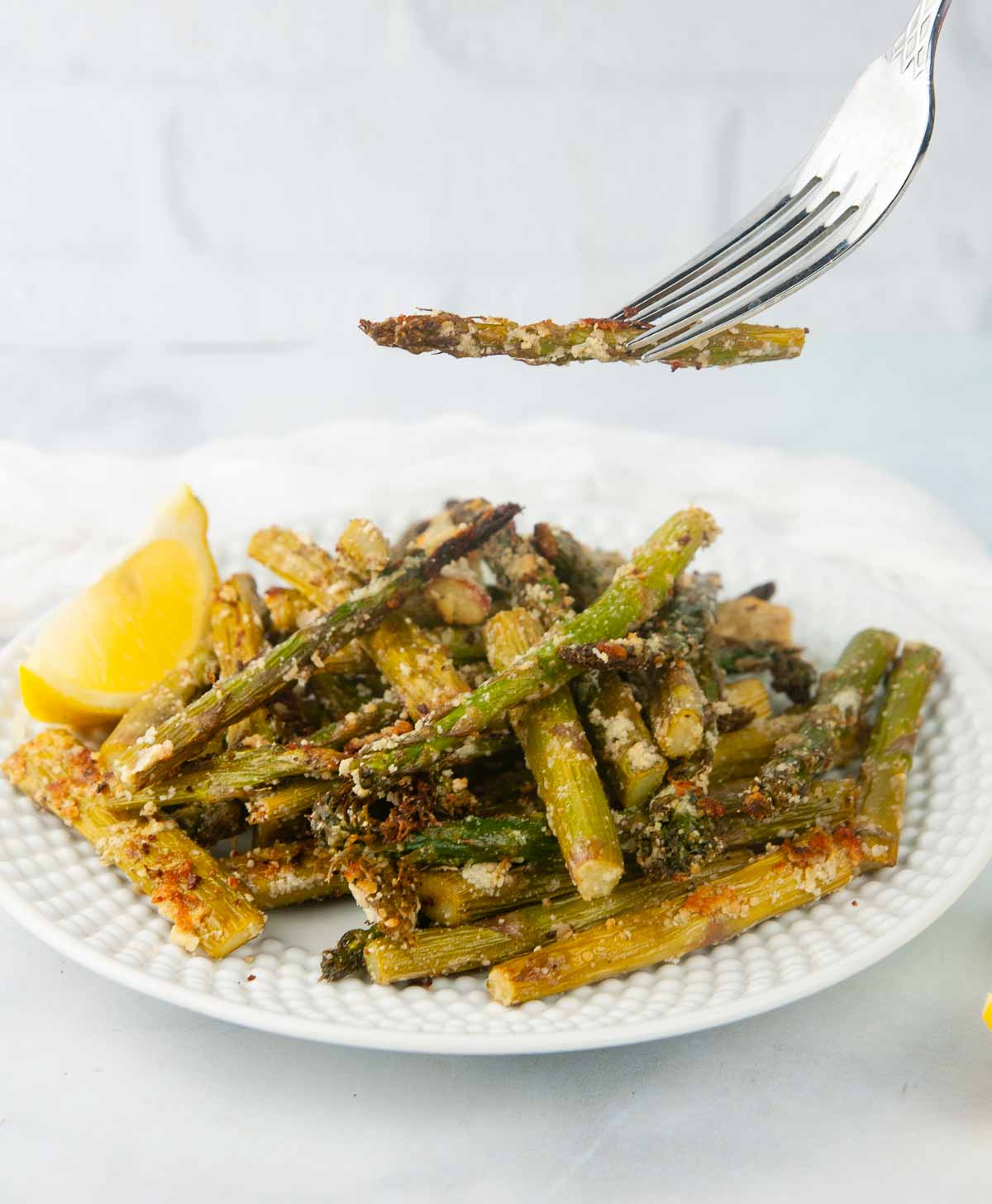 A forkful of air fryer asparagus with parmesan cheese in a white kitchen. It makes the perfect side or light, crispy appetizer.