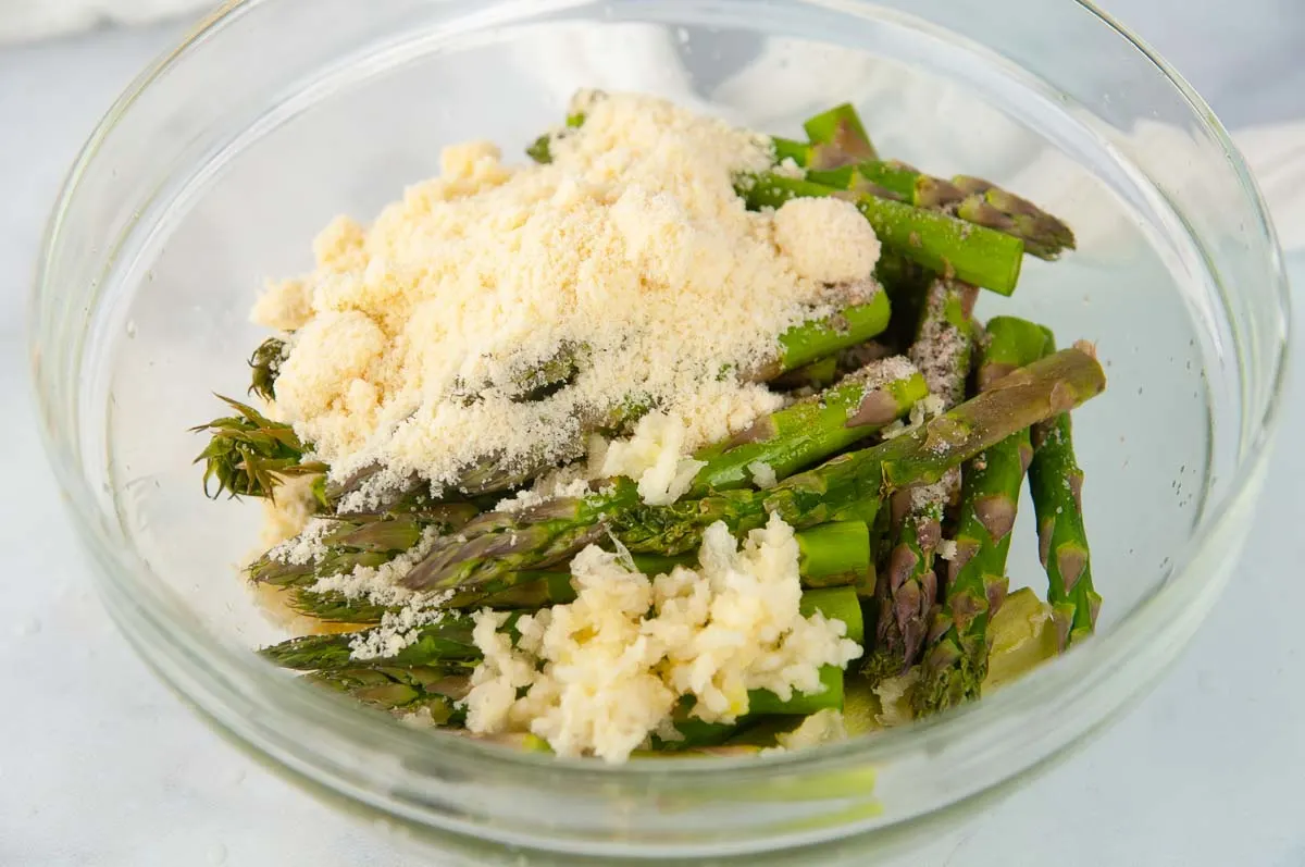 Asparagus in a clear bowl with parmesan cheese, lemon juice, olive oil, and seasoning