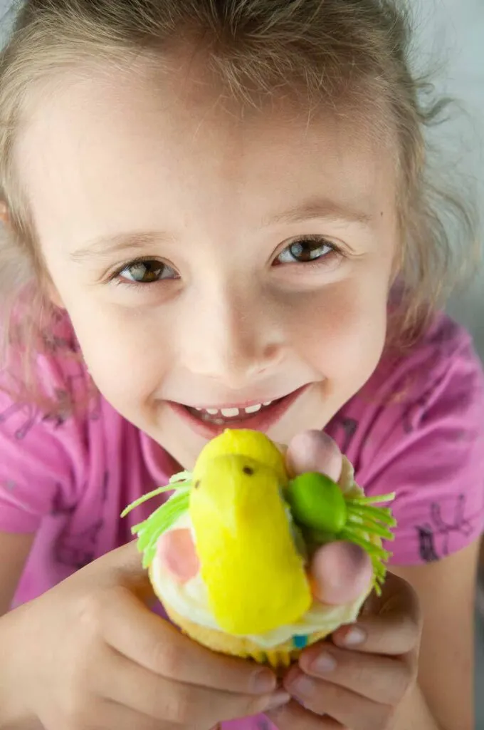 Little girl holding a decorated Easter cupcake and smiling