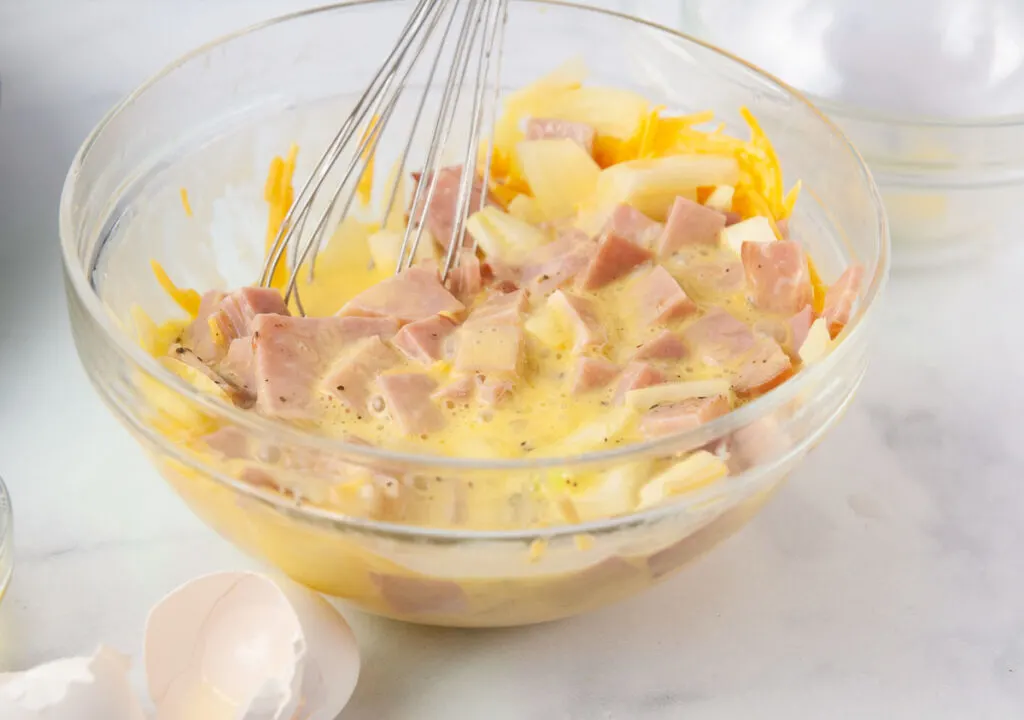Fold in the ham and cheese- ingredients being whisked together in a glass bowl